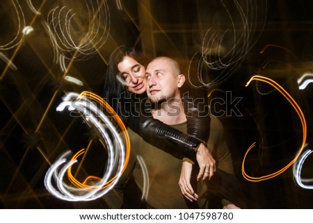 young stylish modern couple of young beautiful women wiht long dark hair and handsome man are kissing, have fun, jocking, hugging, laughing on the street at night