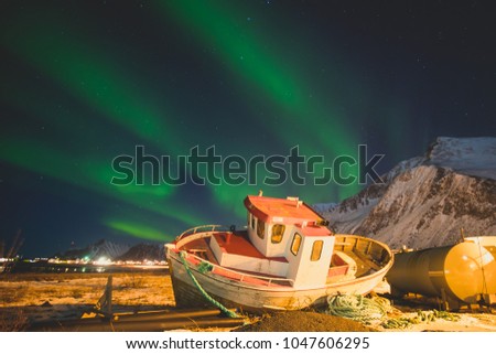 Beautiful picture of massive multicolored green vibrant Aurora Borealis, Aurora Polaris, also know as Northern Lights in the night sky over Norway with the small fishing boat ship, Lofoten Islands
