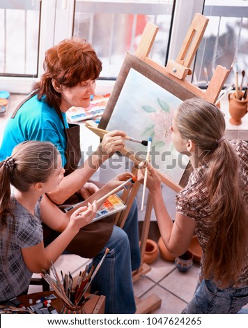 Artist painting easel in studio. Authentic grandmother and kids girl paints with palette watercolor paints palette and brush sunlight. Students taught older woman draw. Elderly professional artist.