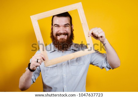 Cheerful smiling bearded man looking through wooden frame