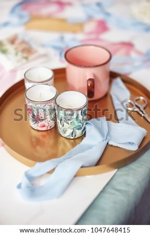 Spring inspiration, texture, pink cup on the table, ribbons, scissors, candles on a golden plate
