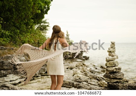 young woman twirling outside with stacked stones by water