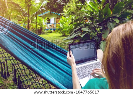 girl lying in a hammock and working on a laptop at the garden
