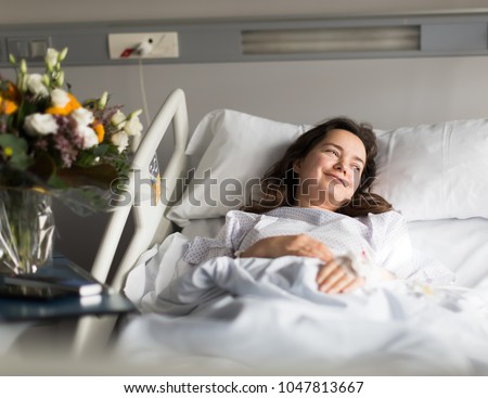 Adult woman is satisfied of visit her and lying on the bed in hospital indoor Royalty-Free Stock Photo #1047813667
