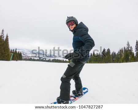 A young man in sports glasses is riding a snowboard in the mountains in Transcarpathia, Ukraine.