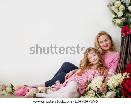 Young beautiful mother and cute daughter are sitting embracing on a white background with flowers. Spring