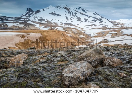 Colourful canyon in Hveradalir geothermal volcanic area, Iceland. Panorama landscape photo of nice valley with volcano mountains covered by snow in background and rounded shape boulders in the front.