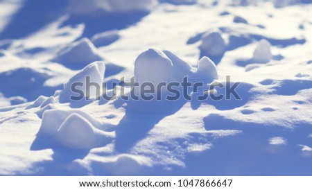 A close-up of the snow on a sunny day against the light.  Pieces of snow sparkle in the light and cast beautiful blue shadows.  The play of light and shadows forms the landscape.  A calm view.
