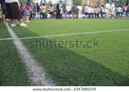 green artificial grass field with white border line and out of focus people standing in the background 