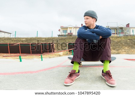 A teenage boy is sitting on a skateboard in the park. The concept of free time pastime for teenagers in the city