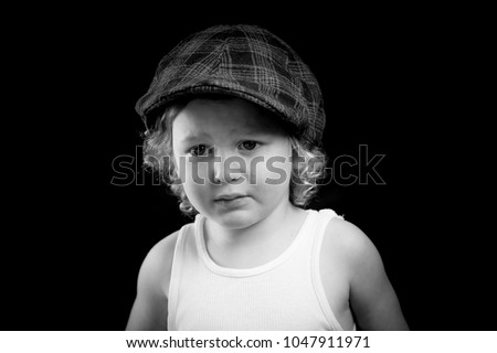 A black and white portrait of a little boy wearing a white tank top crying from one eye. The child has a single tear running down his cheek. The sad child cries from his eyes. There is room for text. 