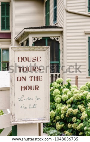 Sign near late 19th-century farmhouse on living history farm in northern Illinois, USA: "House tours on the hour. Listen for the bell." Foreground focus.