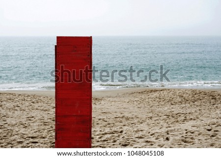 Red wooden lonely pillar at the sea with footprints on a sand and the sea. Concept of loneliness.