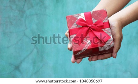 Woman holding a gift box for Christmas or new year and valentine day or anniversary on vintage blue wall background.
