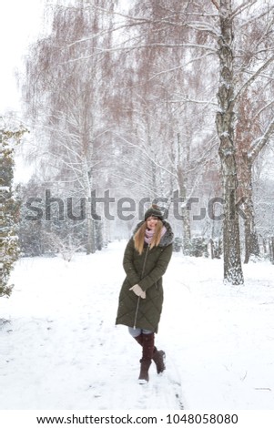 Beautiful girl standing in a park, winter landscape, it's snowing.