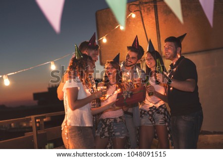 Group of young friends having a birthday party at a building rooftop, singing a song and blowing a candle. Focus on the people in the middle