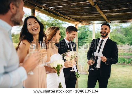 Best man giving speech to newlywed couple at wedding reception. Group of friends gathering for wedding reception. Royalty-Free Stock Photo #1048139134