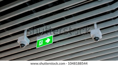Green emergency exit sign. Direction to the escape way and CCTV hanging on wood ceiling.