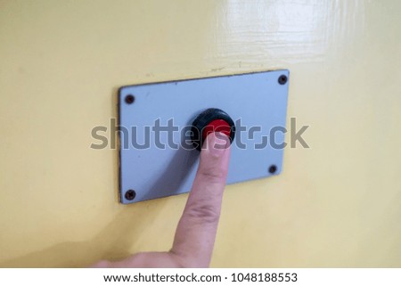 A finger reaches for pressing the red button on yellow background