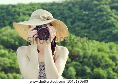 Girl in hat takes pictures against the background of green forest. Front view