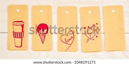 five recycled paper tags with cute pink drawing on white wooden background