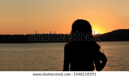 Girl silhouette in sunset time near sea with beautiful nature mountain landscape and orange colors 