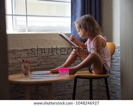 Child girl drawing by watercolor at home. Gentle image with cute little artist draws by herself near the window at kitchen area.