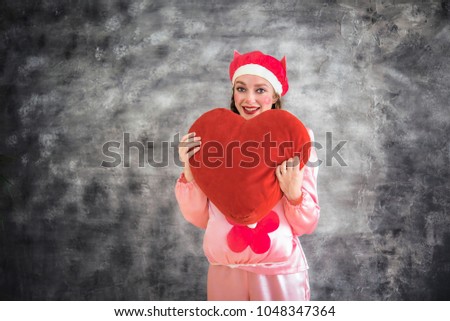 Young cheerful girl in a bright pink suit with a big red heart in hands on a gray background. Animator, costume show, carnival. Bright picture for a poster, bright cheerful card. Carnival costume pig.