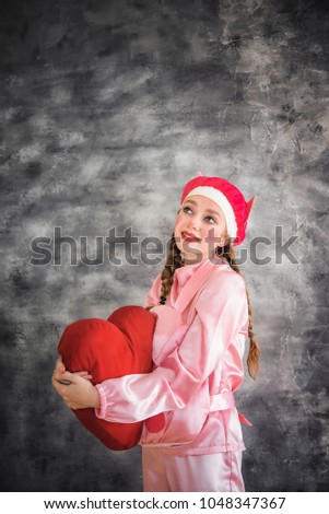 Young cheerful girl in a bright pink suit with a big red heart in hands on a gray background. Animator, costume show, carnival. Bright picture for a poster, bright cheerful card. Carnival costume pig.