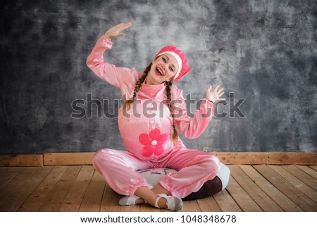 Young cheerful girl in a bright pink suit with a flower on her belly on grey background. Children's animator, costume show, carnival. Bright picture for a poster, cheerful card. Carnival costum pig.