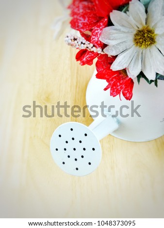 Top view image of white metal shower bucket decorated with artificial white and red flowers placed on wooden table with bright blurred space for add 