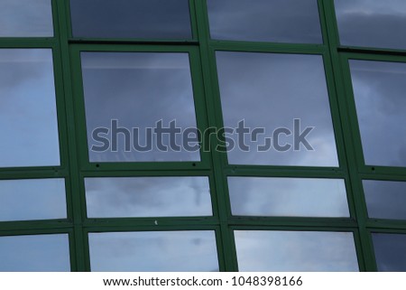 Outdoor view of a modern wall made of polygonal glass windows. Pattern of reflective flat surfaces and green lines. Modern design. New building facade. Geometric image. Abstract architectural picture.
