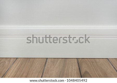 Light matte wall, white baseboard and tiles immitating hardwood flooring Royalty-Free Stock Photo #1048405492