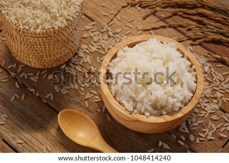 Jasmine rice in wood bowl and paddy rice on a brown wooden background beautiful Thai food Royalty-Free Stock Photo #1048414240