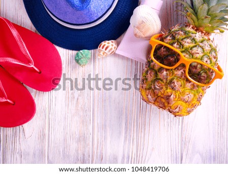 Summer holiday composition - pineapple, hat, flip flops, sun protection cream, over wooden background