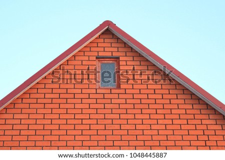 The roof of a house made of red brick with a window on the sky background