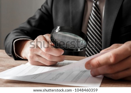 Businessman holding magnifying glass zoom and analyzing financial indicators Royalty-Free Stock Photo #1048460359