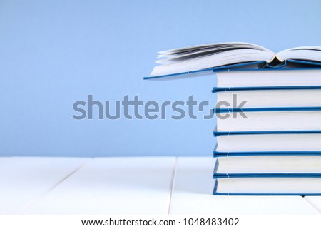 A stack of books on a blue background. One hidden book on top of the pile