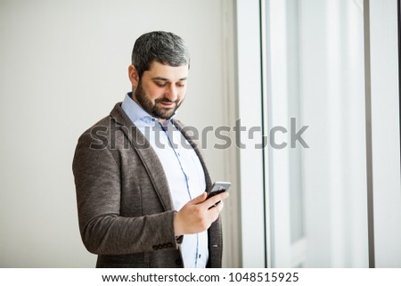 Man holding phone - young businessman using smartphone in office. Casual urban professional business man texting cellphone happy inside office banner panorama with copy space on background