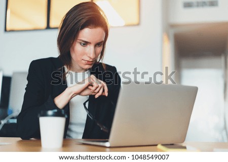 Pensive beautiful businesswoman using laptop computer at modern office.Blurred background.Horizontal