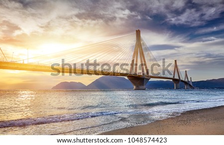 Sunset view on the bridge near Patras. Suspension bridge crossing Corinth Gulf strait, Greece, Europe. Second longest cable-stayed bridge in the world. Dramatic red sky under a Rion-Antirion Bridge.  Royalty-Free Stock Photo #1048574423