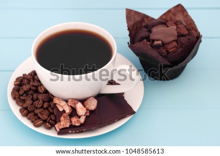 White cup with coffee and chokolate cupkake on a turquoise wooden background.