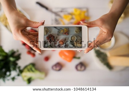Hands with the phone close-up pictures of meal. Young woman, cooking blogger is cooking at the home kitchen in sunny day and is making photo at smartphone. Instagram food blogger workshop concept.