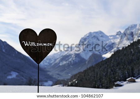 A iron heart shaped welcome sign with white snow covered mountains in the background, Bavarian Alps, Germany.