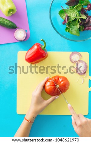Woman cooking summer vegetarian salad on blue background. Healthy food concept