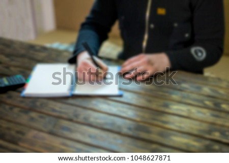 Freelancer works at the desk making notes in a notebook at home. Blur, blurred image, background image.