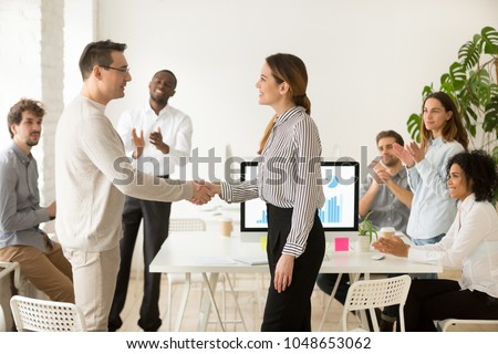 Smiling female boss promoting rewarding handshaking motivated worker showing respect while team applauding congratulating colleague at group meeting, appreciation and employee recognition concept Royalty-Free Stock Photo #1048653062