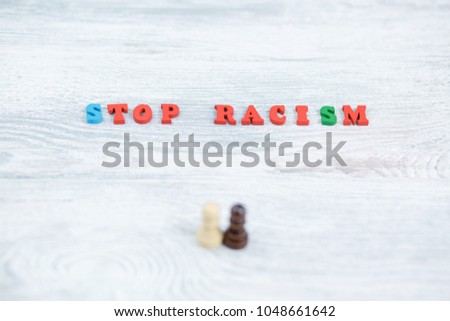 No to racism in colored letters on a gray wooden background, black and white pawn, the concept of the struggle for freedom of human rights