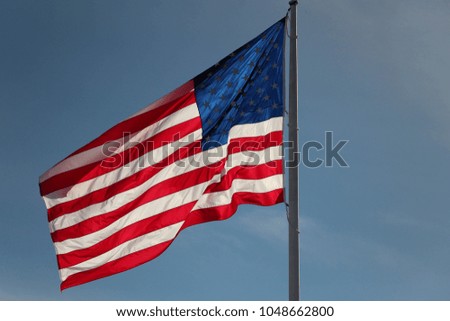 american flag billowing in the wind against a blue sky 