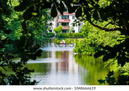 Amazing parks of Bremen, Germany. Natural trees frame surrounding the composition of the shot. There is a tiny red cabin in the middle of the lake.